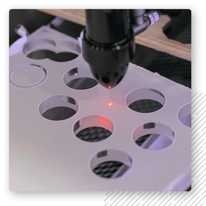 Laser wycinający okrągłe krążki w płycie plexi, widoczny czerwony punkt wiązki
