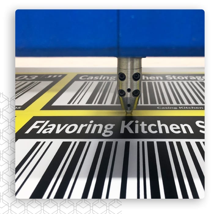 Ploter tnący nad wydrukiem z napisem Flavoring Kitchen, żółtym pasem i kodami kreskowymi