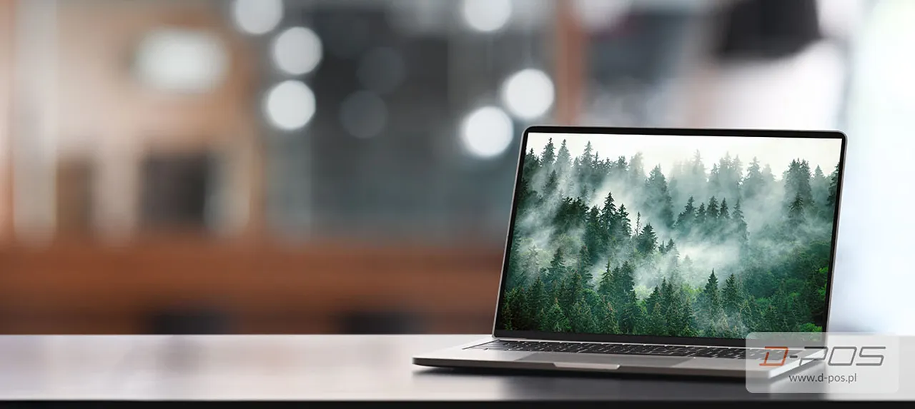 Laptop na biurku z motywem mglistego iglastego lasu wyświetlonym na ekranie