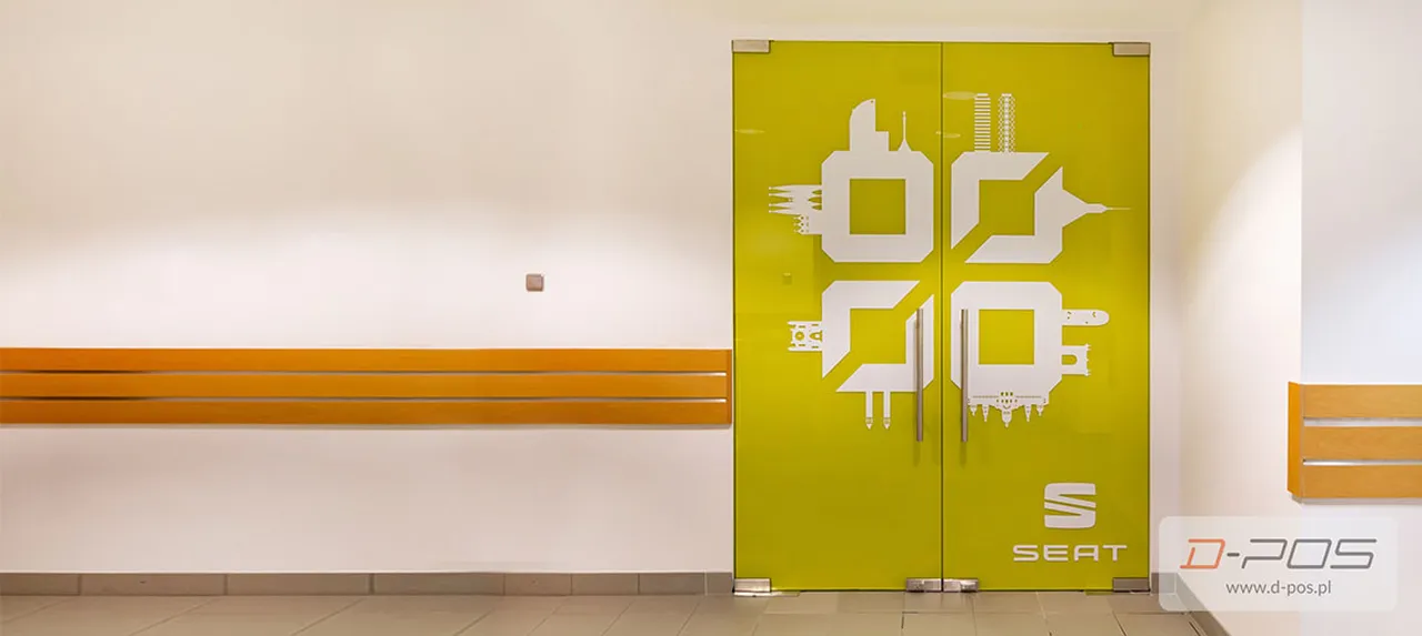 Żółte szklane drzwi z białą grafiką przy recepcji jako reklama indoor