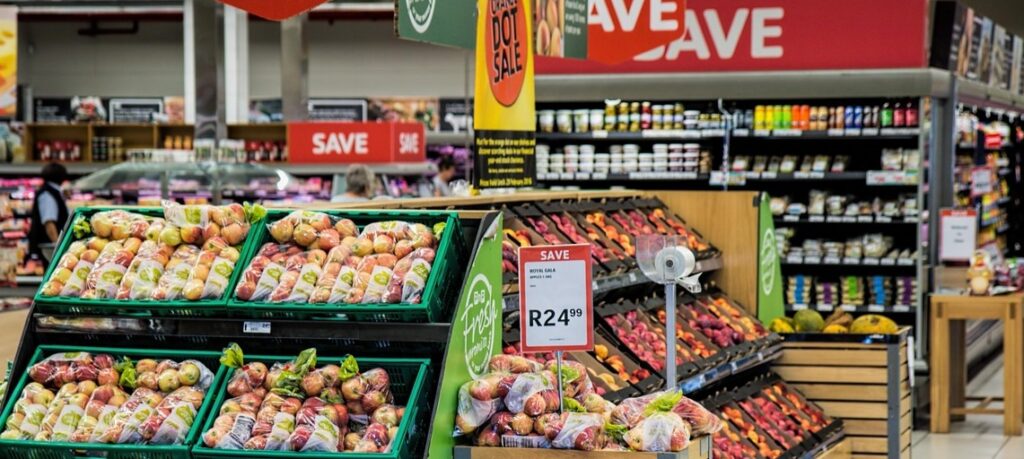 Sklepowa ekspozycja warzyw i owoców z czerwonymi cenówkami promocyjnymi