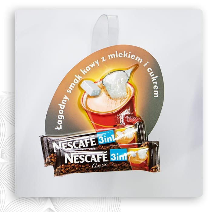 Wobbler reklamowy z grafiką kawy zawieszony nad saszetkami Nescafé