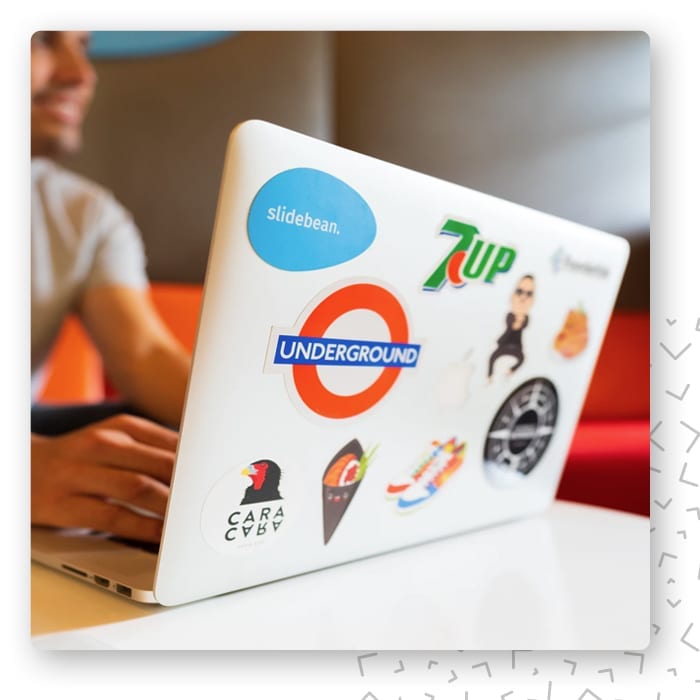 Laptop oklejony naklejkami z logo 7UP i znakiem londyńskiego metra