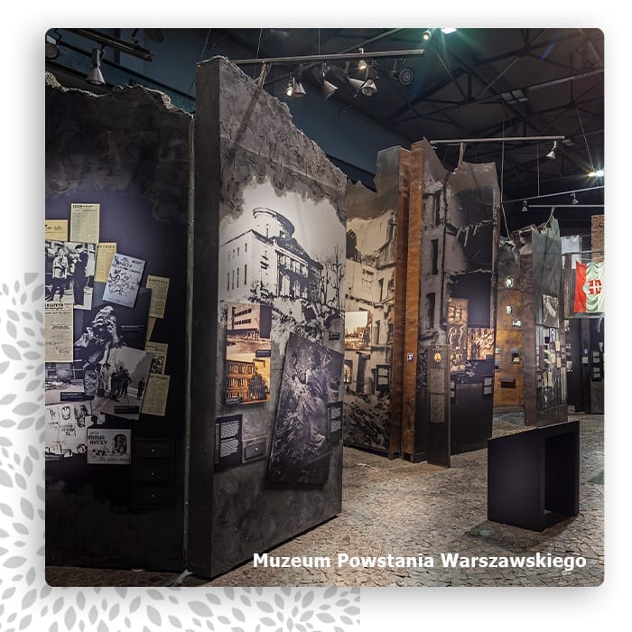 Ciemna sala Muzeum Powstania Warszawskiego z rekonstrukcją ulicy i archiwalnymi fotografiami
